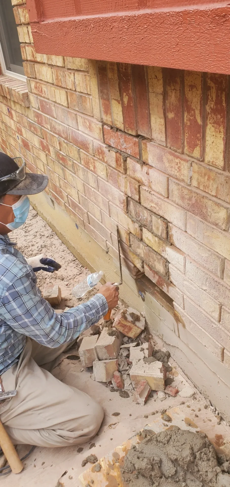 A man in plaid shirt and hat working on brick wall.