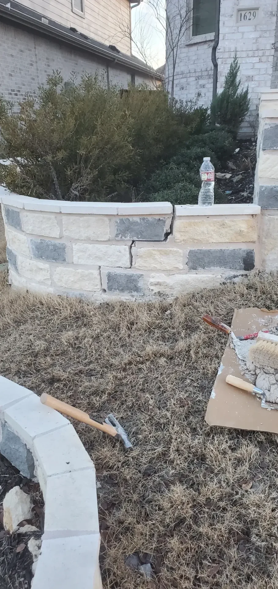 A brick wall with mortar and some tools on the ground